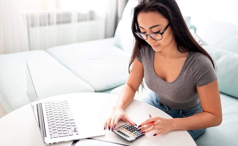 Asian woman using calculator and laptop for calaulating home budget finance taxes