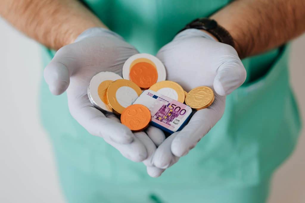 A person in a green scrub suit is holding a small box filled with coins, showcasing a moment of care and attention.